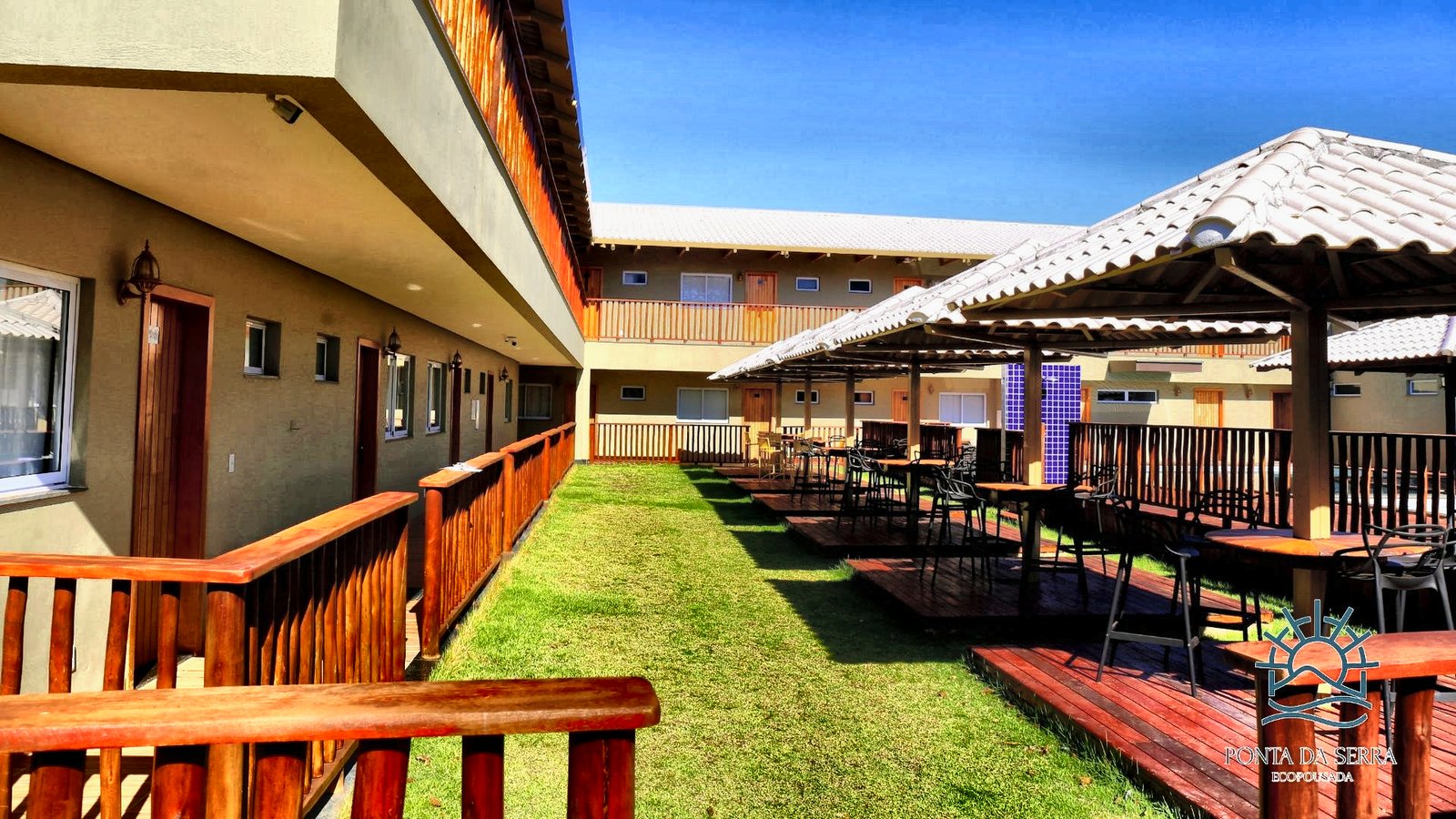 Pátio interno com gramado, decks de madeira e os apartamentos em dois andares